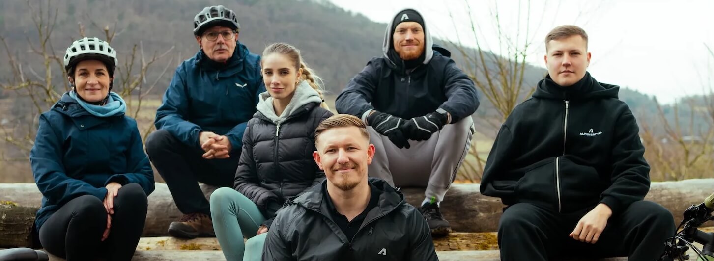 Das Alpensattel-Team sitzt gemeinsam draußen auf einem Baumstamm